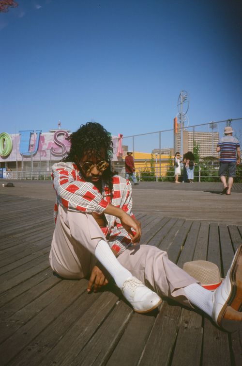 Free Man in stylish casual wear with curly hair sitting on a boardwalk, wearing sunglasses. Stock Photo