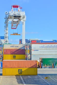 Stacked cargo containers in a sunny port industrial setting with crane.