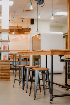 Modern dining area with industrial elements, featuring wooden tables and metal stools under hanging lights.