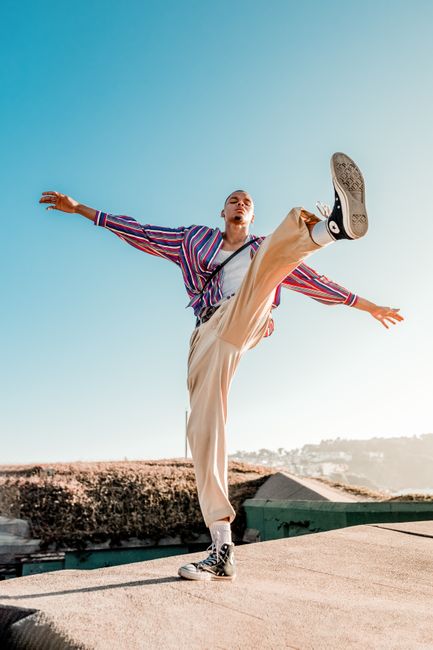 Man in stylish outfit poses dynamically on a rooftop under clear blue skies.