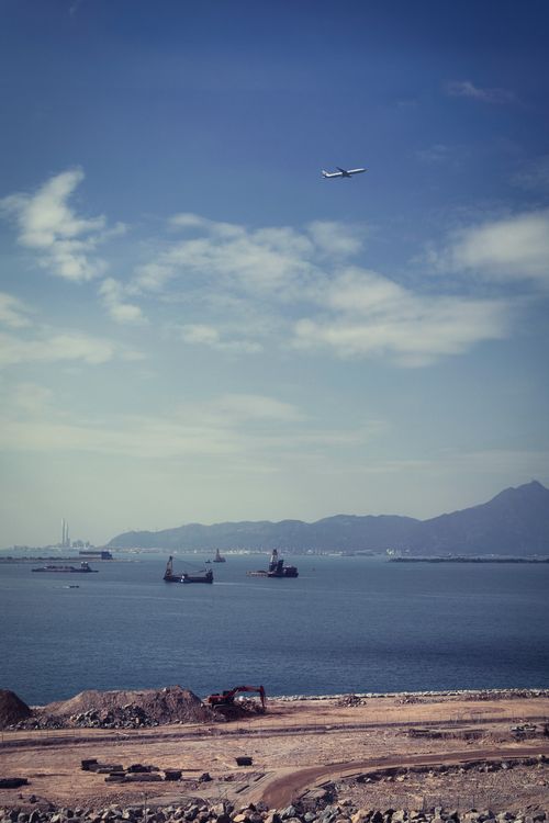 Free An airplane flies over a coastal scene with construction and distant mountains. Stock Photo