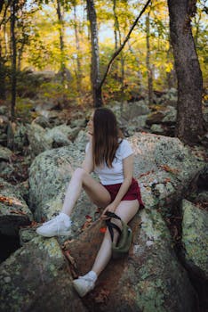 Young woman sitting on a rock in a forest enjoying nature. Ideal for lifestyle and travel themes.