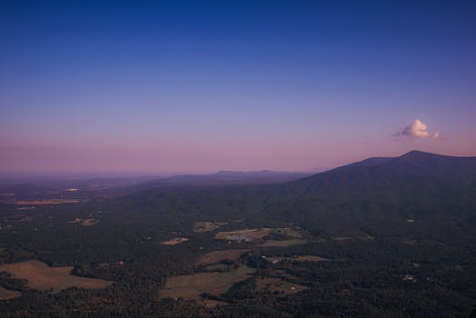 Scenic aerial view of rolling hills and mountains under a vibrant dusk sky.