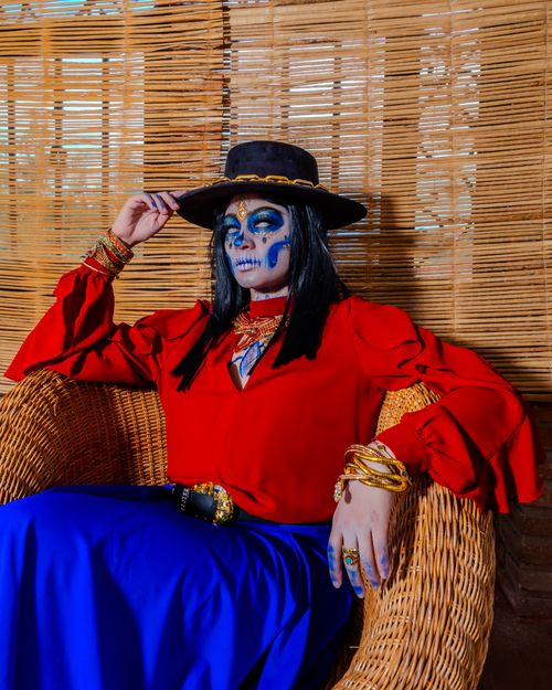 Free Elegant Catrina in traditional Mexican costume with face paint, seated indoors. Stock Photo