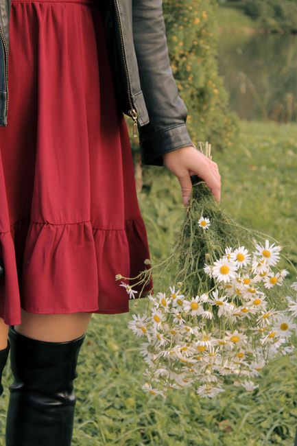 A woman in a red dress holding daisies in a grassy outdoor setting.