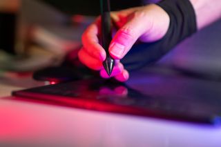 Hand using a stylus on a graphics tablet in colorful light — photo by Jakub Zerdzicki on Pexels