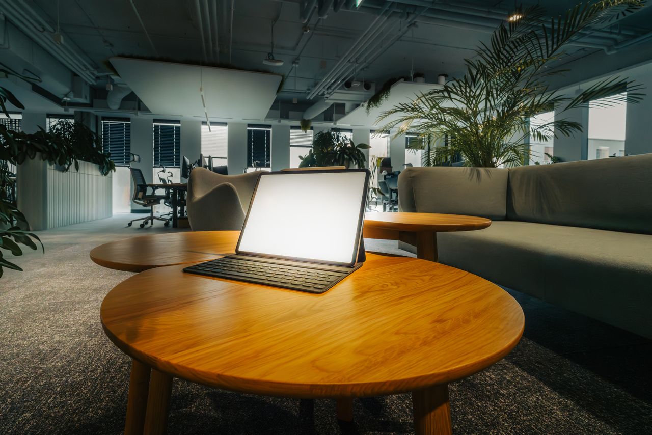 empty office lounge featuring a glowing laptop on a wooden table surro