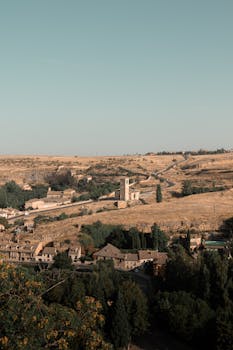 Explore the vast countryside of Segovia, Spain, with rolling fields and historic architecture on a clear summer day.