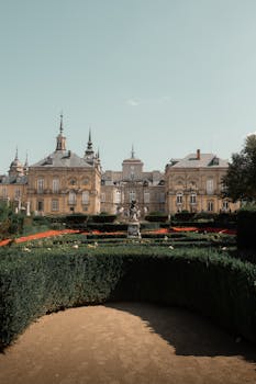 Explore the grandeur of Segovia Palace, Spain, surrounded by meticulously maintained gardens under a clear sky.