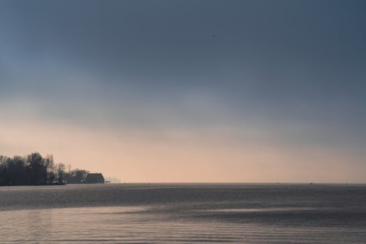 Peaceful scene of a tranquil lake at dusk with soft lighting and trees in silhouette.