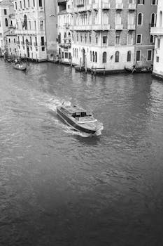 A serene black and white view of a gondola navigating a Venice canal, Italy.