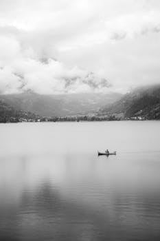 Black and white photo of a canoe on Lake St. Moritz surrounded by misty mountains.