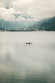 A tranquil scene of a lone boat on a calm lake with mountains in the background.
