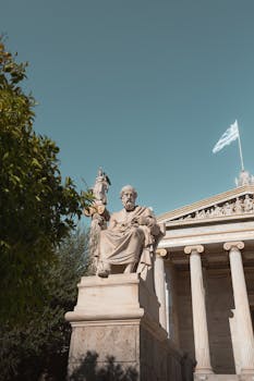 Plato's statue in front of the National Library of Greece against a clear blue sky.