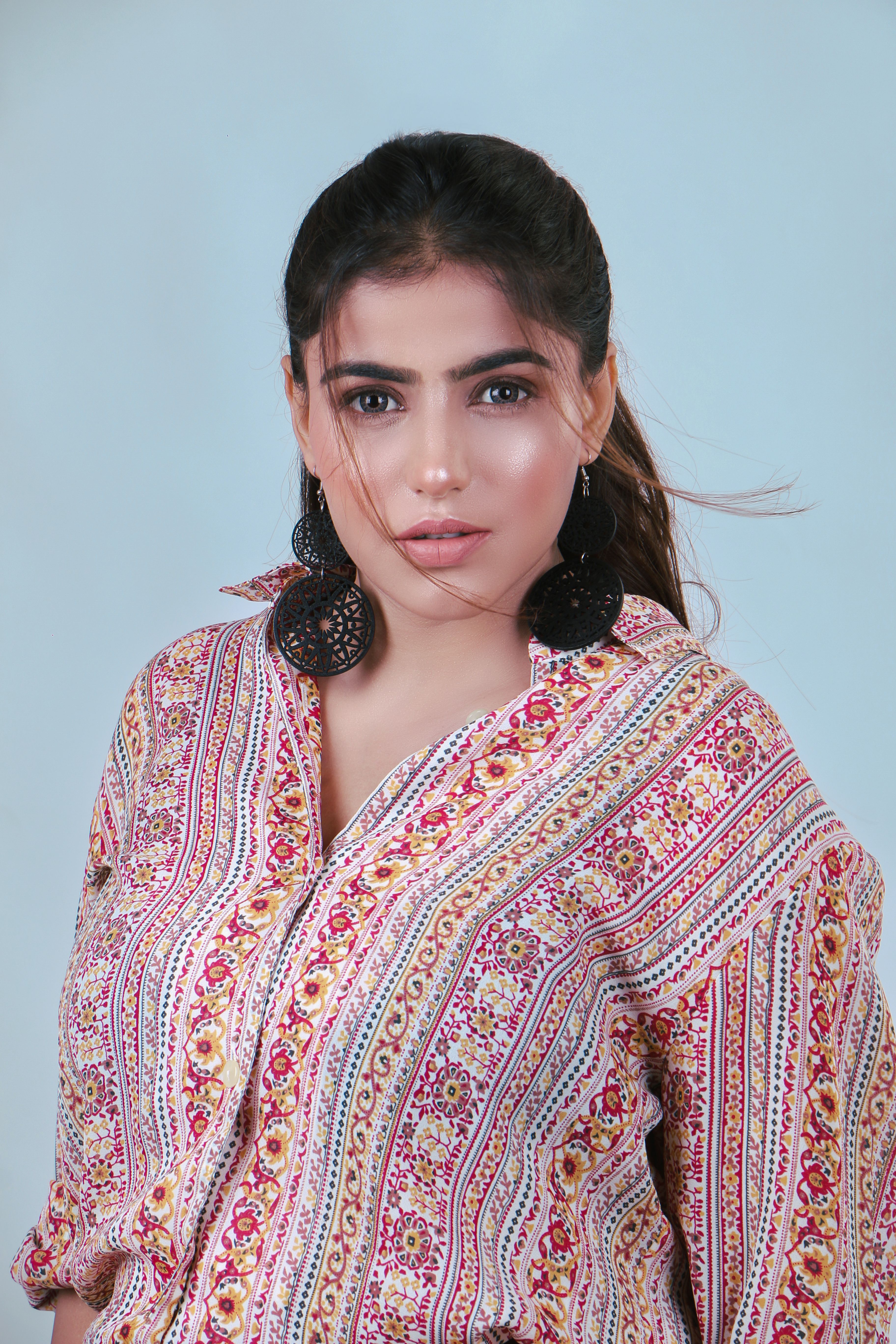 Close-up portrait of a woman wearing a floral shirt and bold earrings against a neutral background.