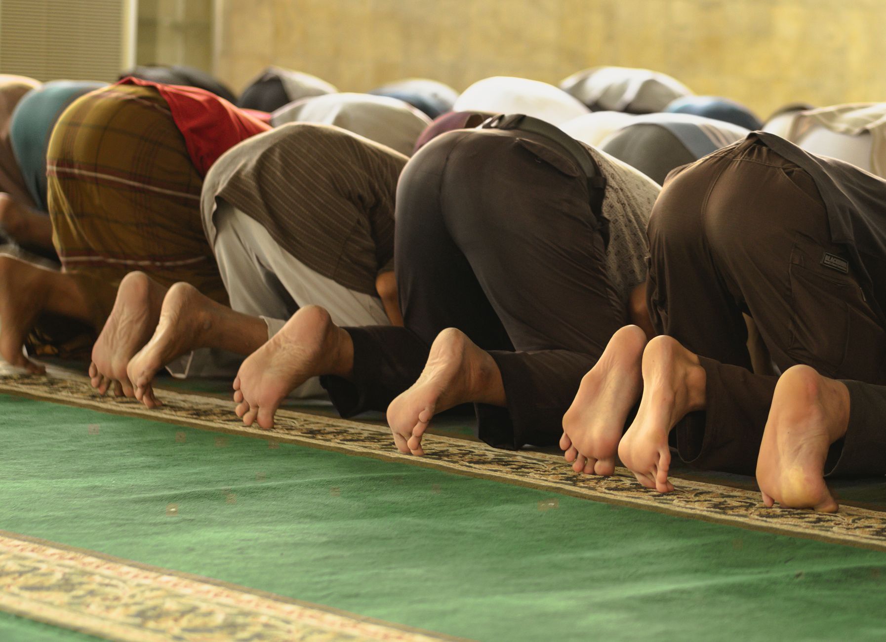 A group of Muslim worshippers praying inside a mosque, captured from behind.