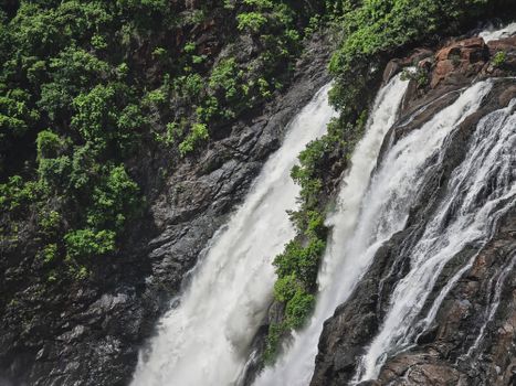 Powerful waterfall cascading amidst dense greenery and rocky terrain.