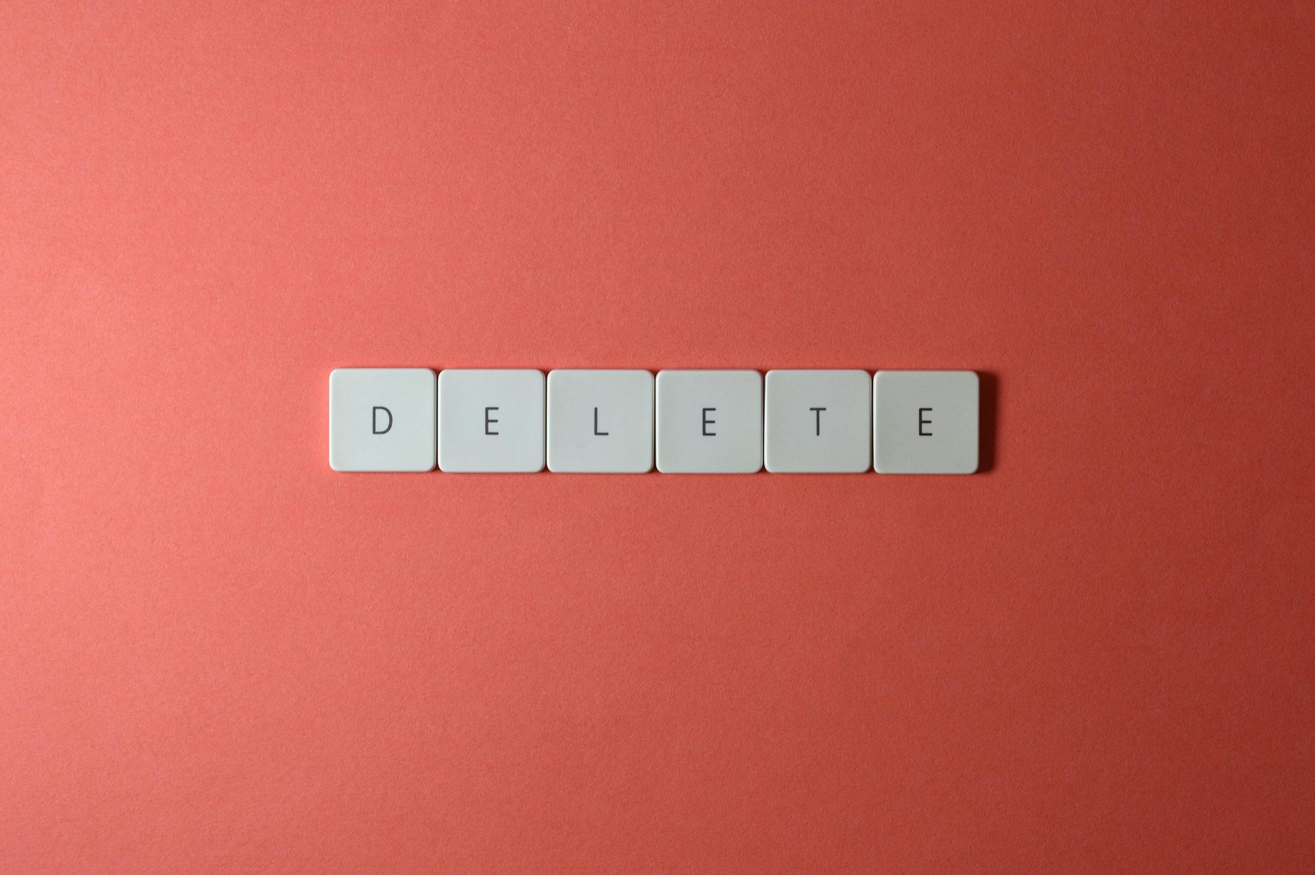 Close-up of keyboard letters spelling 'DELETE' on a coral background, emphasizing digital concepts.