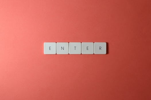Close-up of five keyboard letter tiles spelling 'ENTER', placed on a coral backdrop.