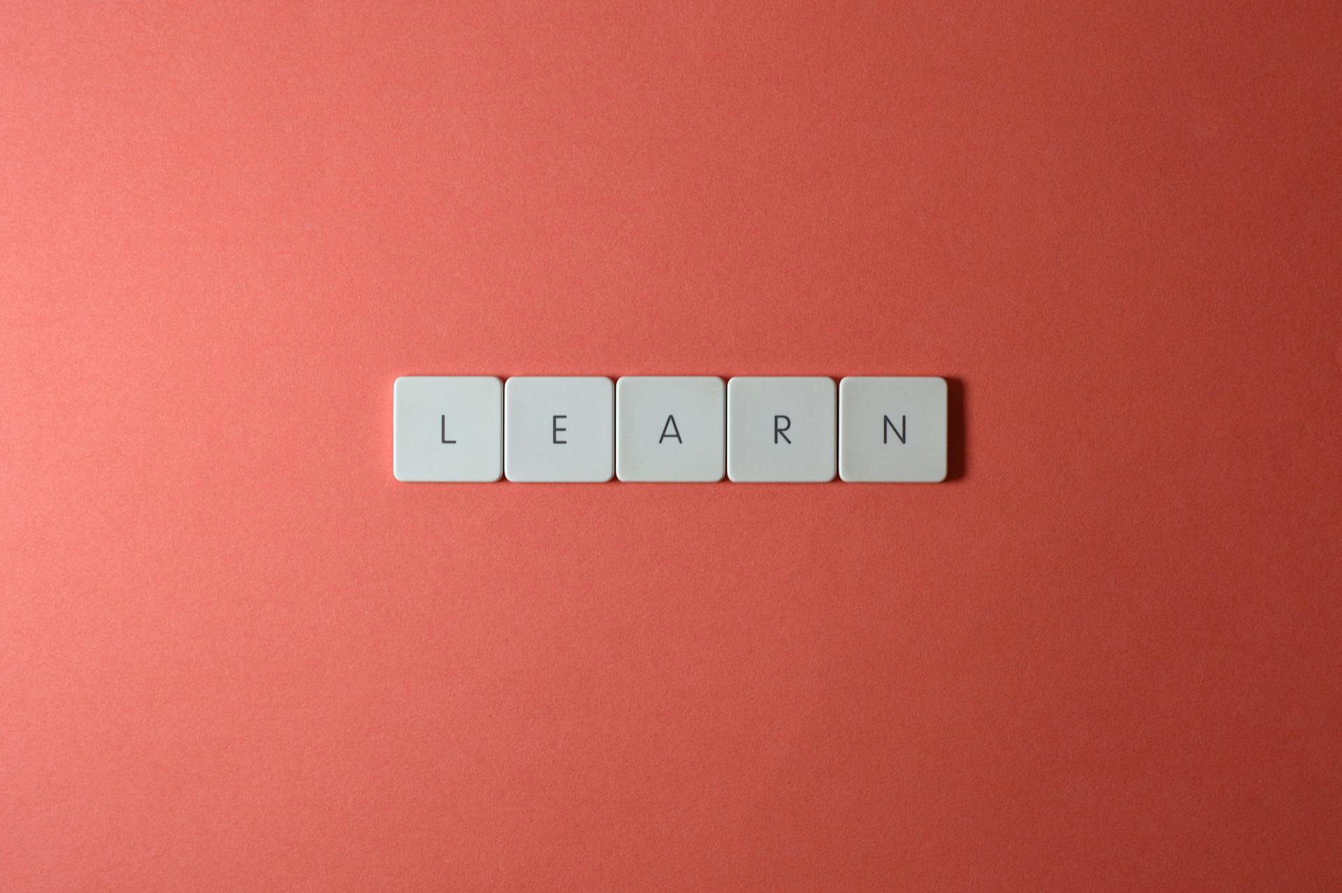 Flat lay of word tiles spelling 'learn' on a coral background, symbolizing knowledge and education.