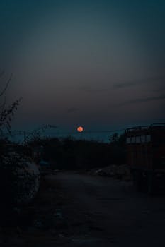 Eerie blood moon above a rural landscape at twilight, capturing a mystical atmosphere.