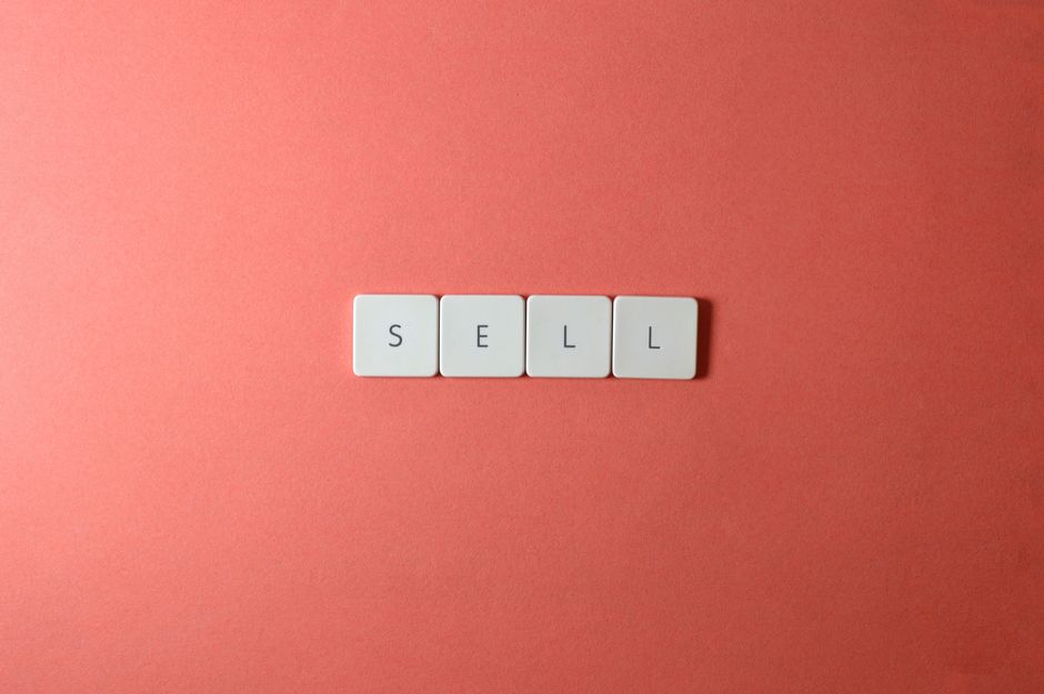 Close-up of keyboard tiles spelling 'sell' on a red background, minimalist design.