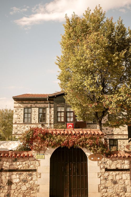 Free A quaint stone house with autumn foliage and a Turkish flag, exuding rustic charm. Stock Photo