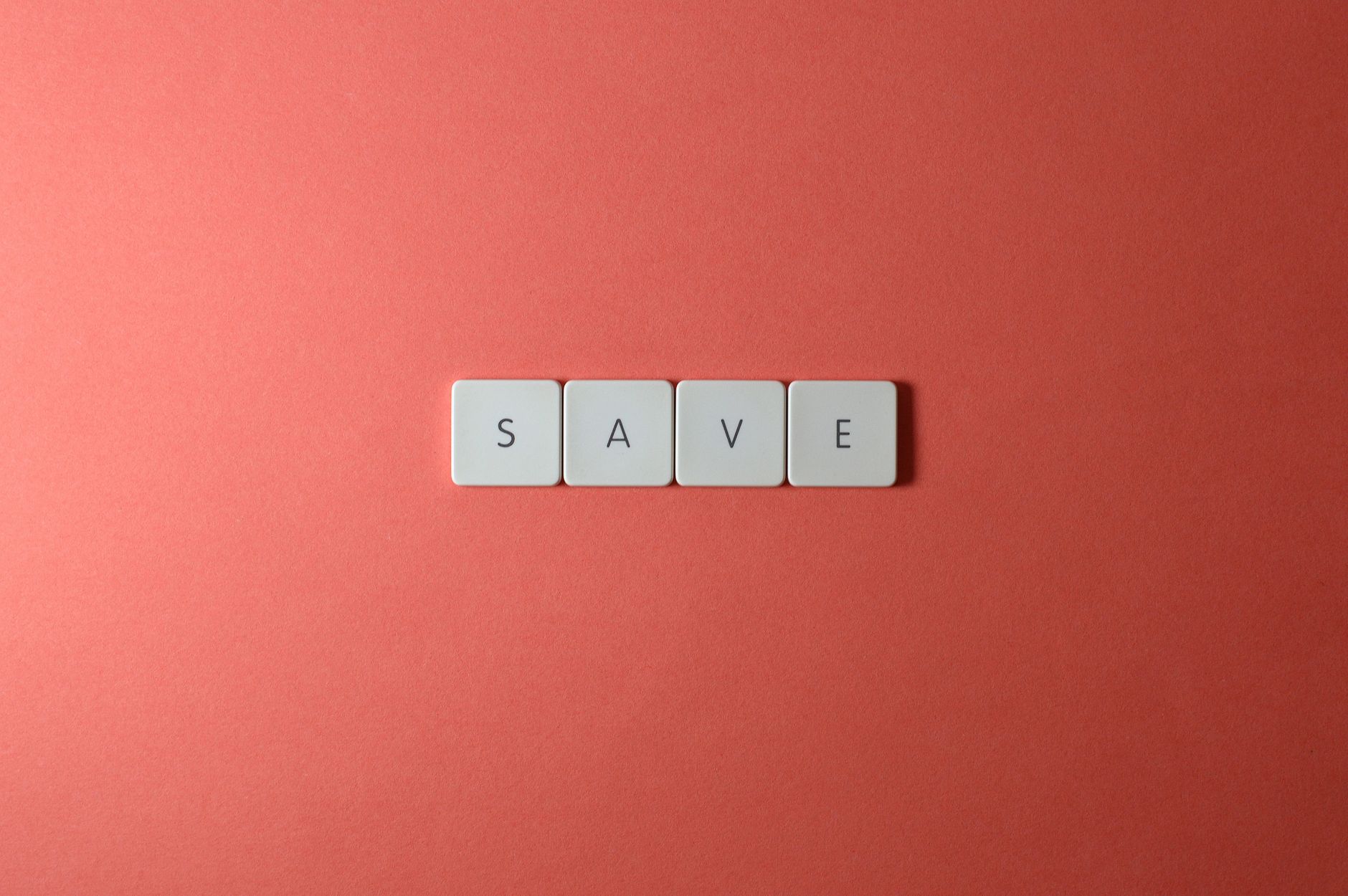 A minimalist flat lay featuring keyboard keys spelling 'SAVE' on a red surface, ideal for conceptual themes.