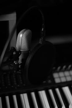 Monochrome image of a microphone and piano keys creating a moody musical ambiance.