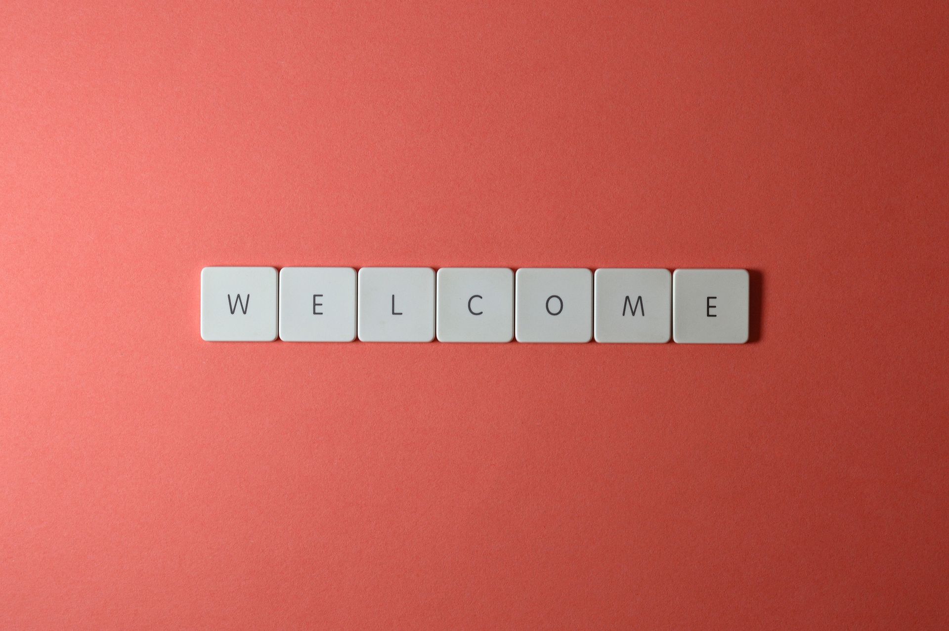 Flat lay of white tiles spelling 'WELCOME' on a red background