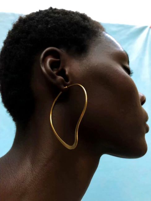 Profile of an adult wearing a modern gold earring against a blue background.