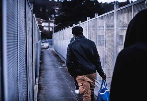 A candid shot of people walking down a narrow urban alleyway lined with metal fences.