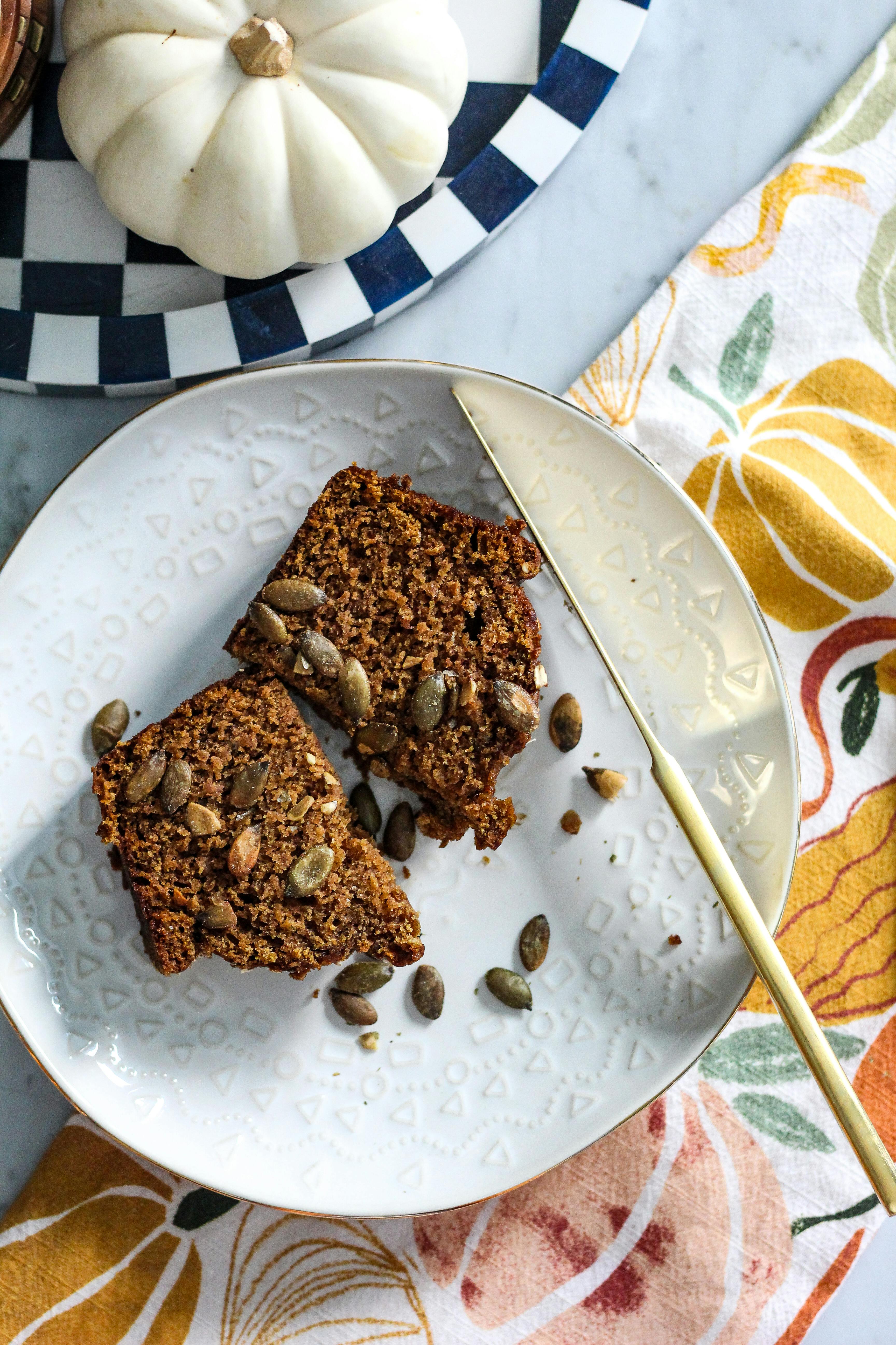 A close-up of two slices of artisan pumpkin bread with seeds, styled with autumn-themed decor.