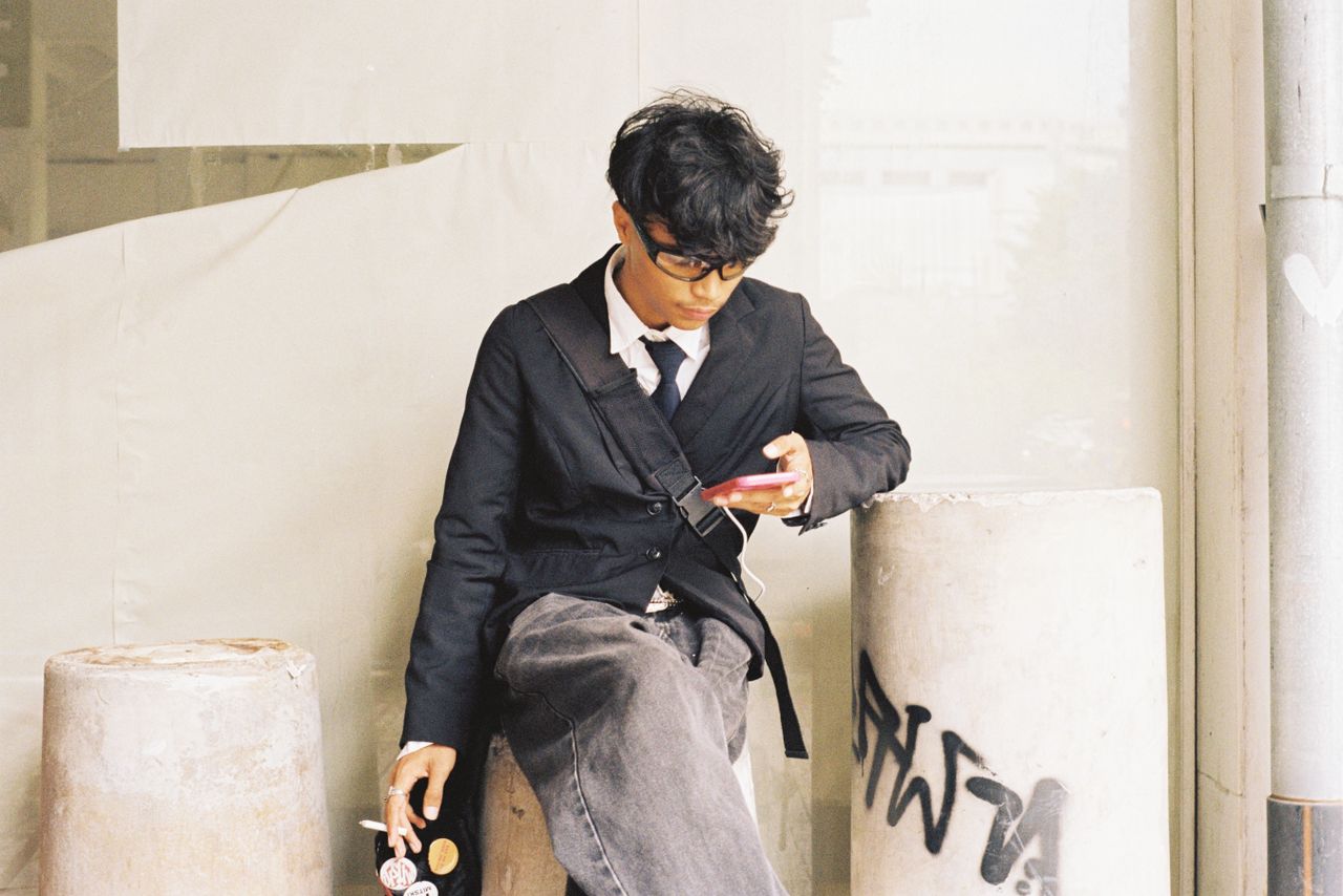 young adult sitting outdoors focusing on a smartphone wearing casual a