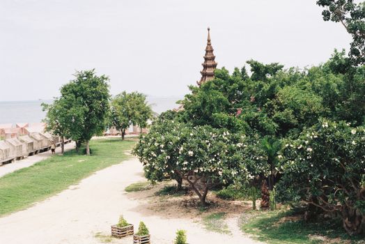 A traditional temple surrounded by lush greenery and a scenic pathway near a waterfront.