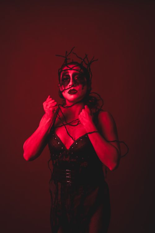 Free Artistic portrait of a woman with dark makeup and branches, in striking red lighting. Stock Photo
