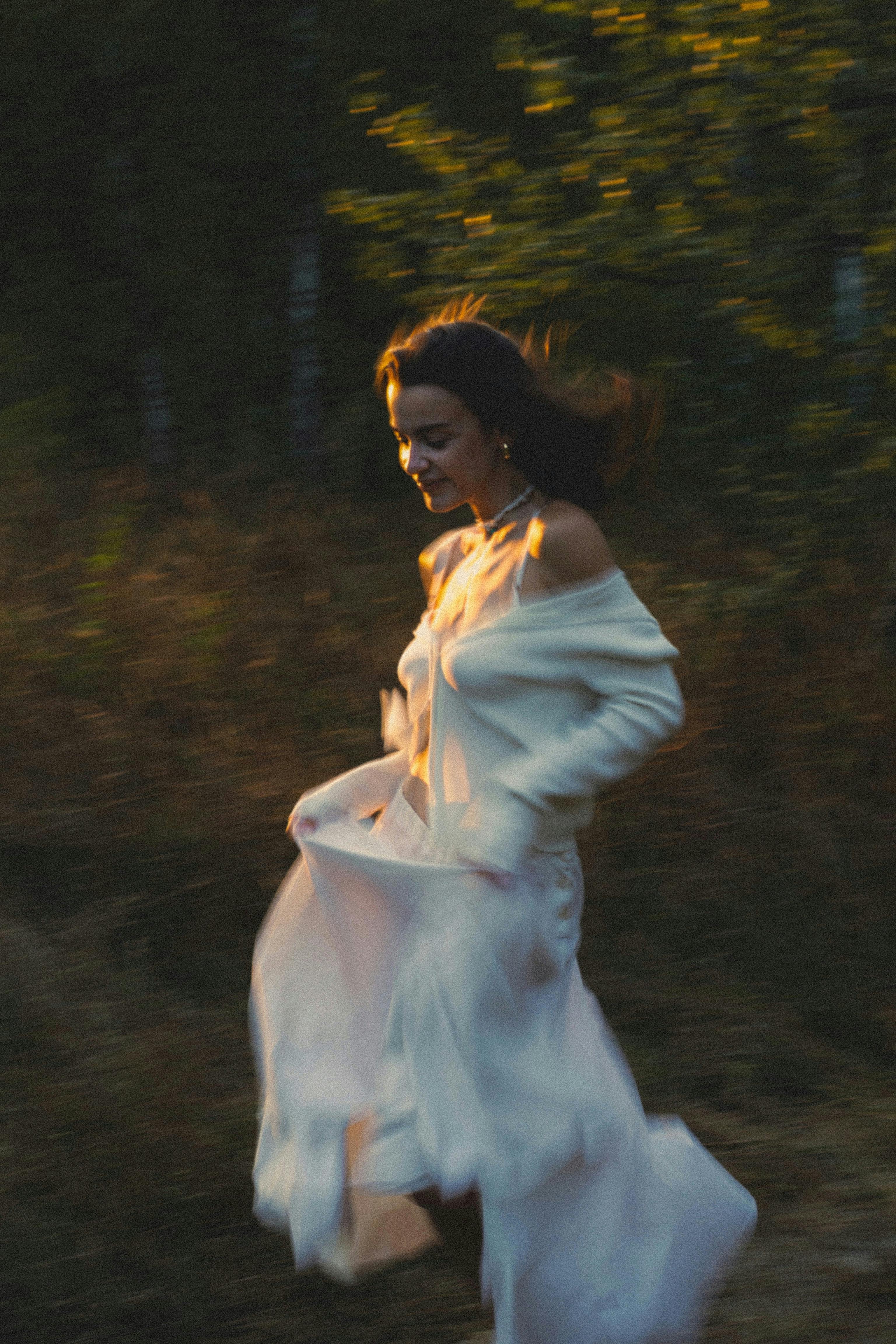Blurred image of a joyful woman in a white dress running outdoors at dusk.