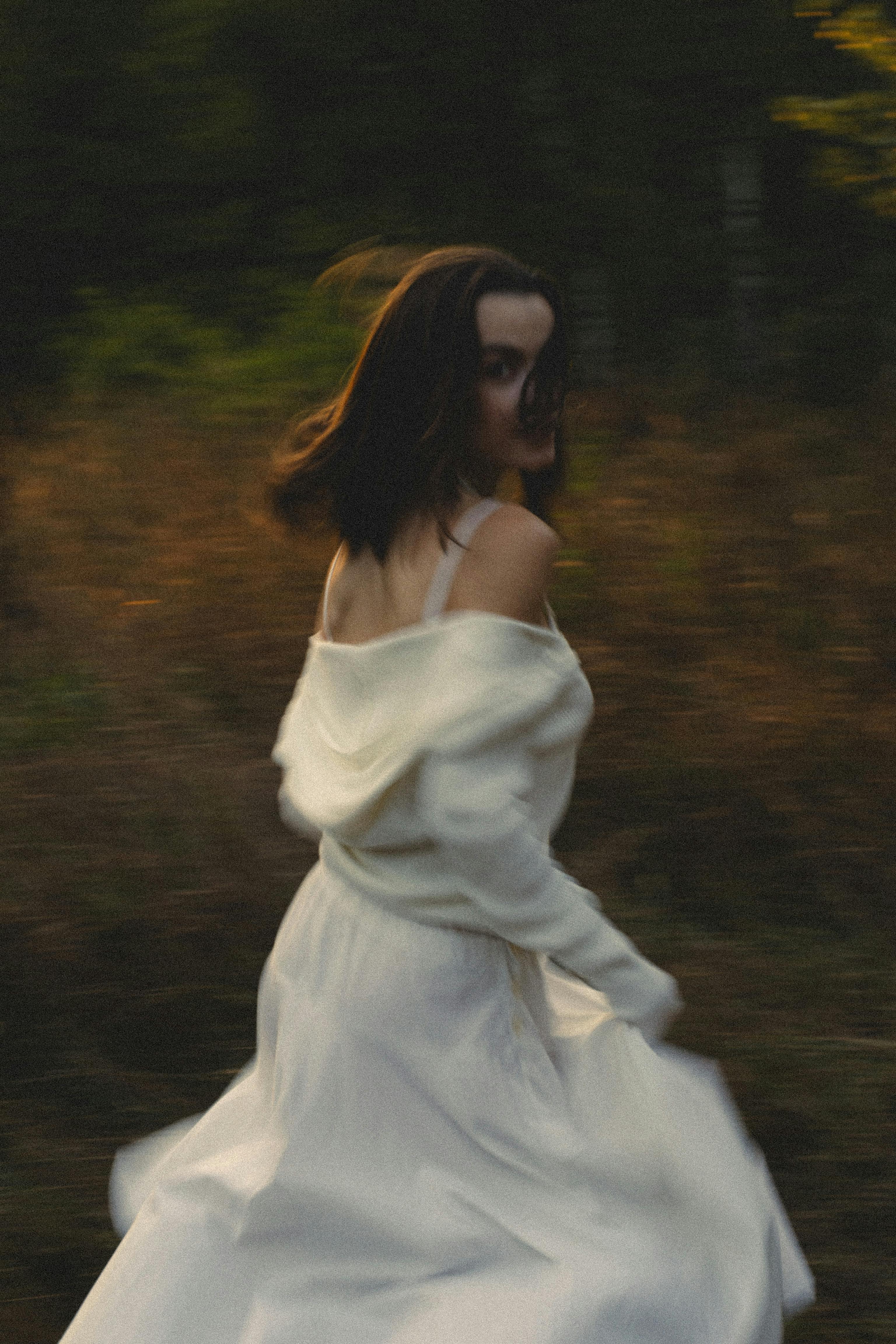 Blurred motion portrait of a woman in a white dress running outdoors.