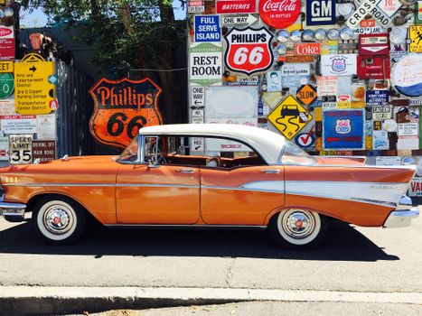 Classic orange car parked by a retro wall with vintage signs under the sun.