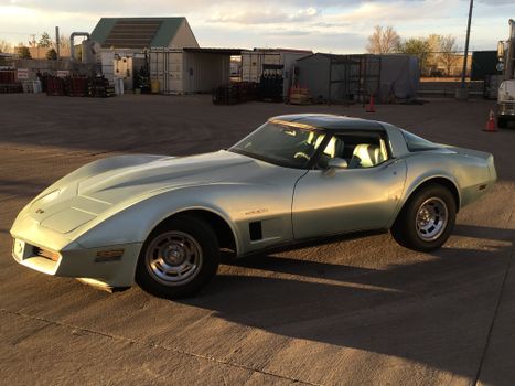 Vintage silver sports car in an industrial yard during sunset, showcasing sleek design and nostalgia.