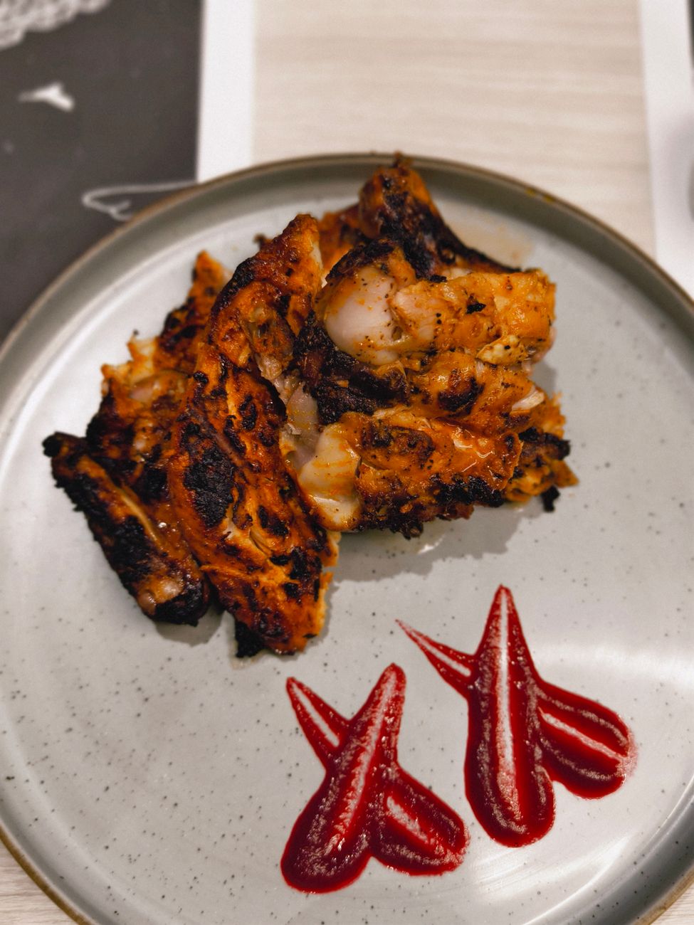 Grilled Jamaican jerk chicken pieces with dark charred skin served with bright orange scotch bonnet pepper sauce on a rustic plate
