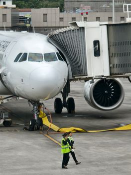 Airplane connected to terminal jet bridge with ground crew walking nearby.
