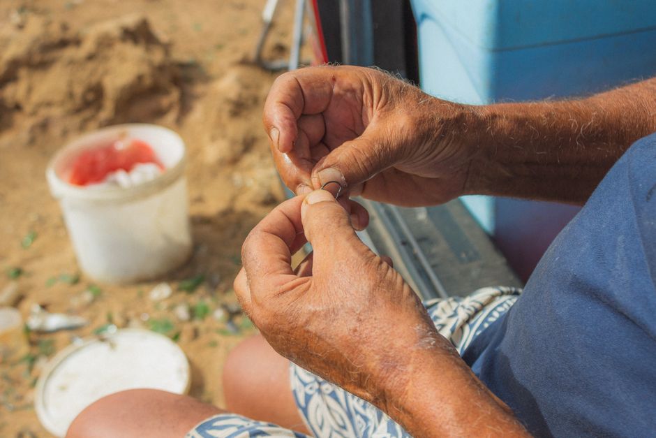 Close-up of a senior man preparing a fishing line on a beach, showcasing skilled hands.