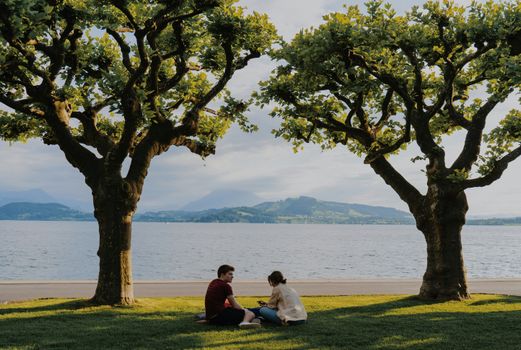 Two people relax by the lake, surrounded by lush greenery and scenic views.