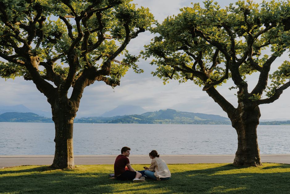 Two people relax by the lake, surrounded by lush greenery and scenic views.