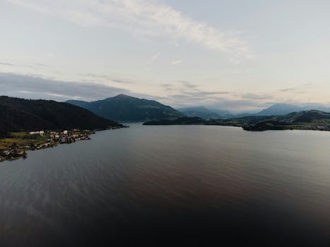 Aerial view of calm mountain lake surrounded by hills at dusk, serene setting.