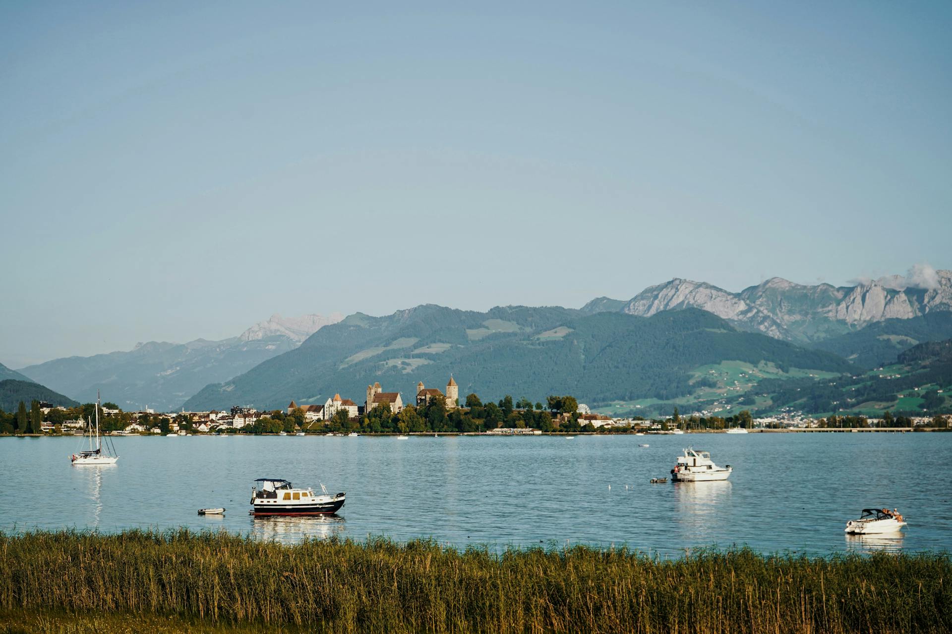 Peaceful lake scene with boats near a Swiss village and mountains in the background.