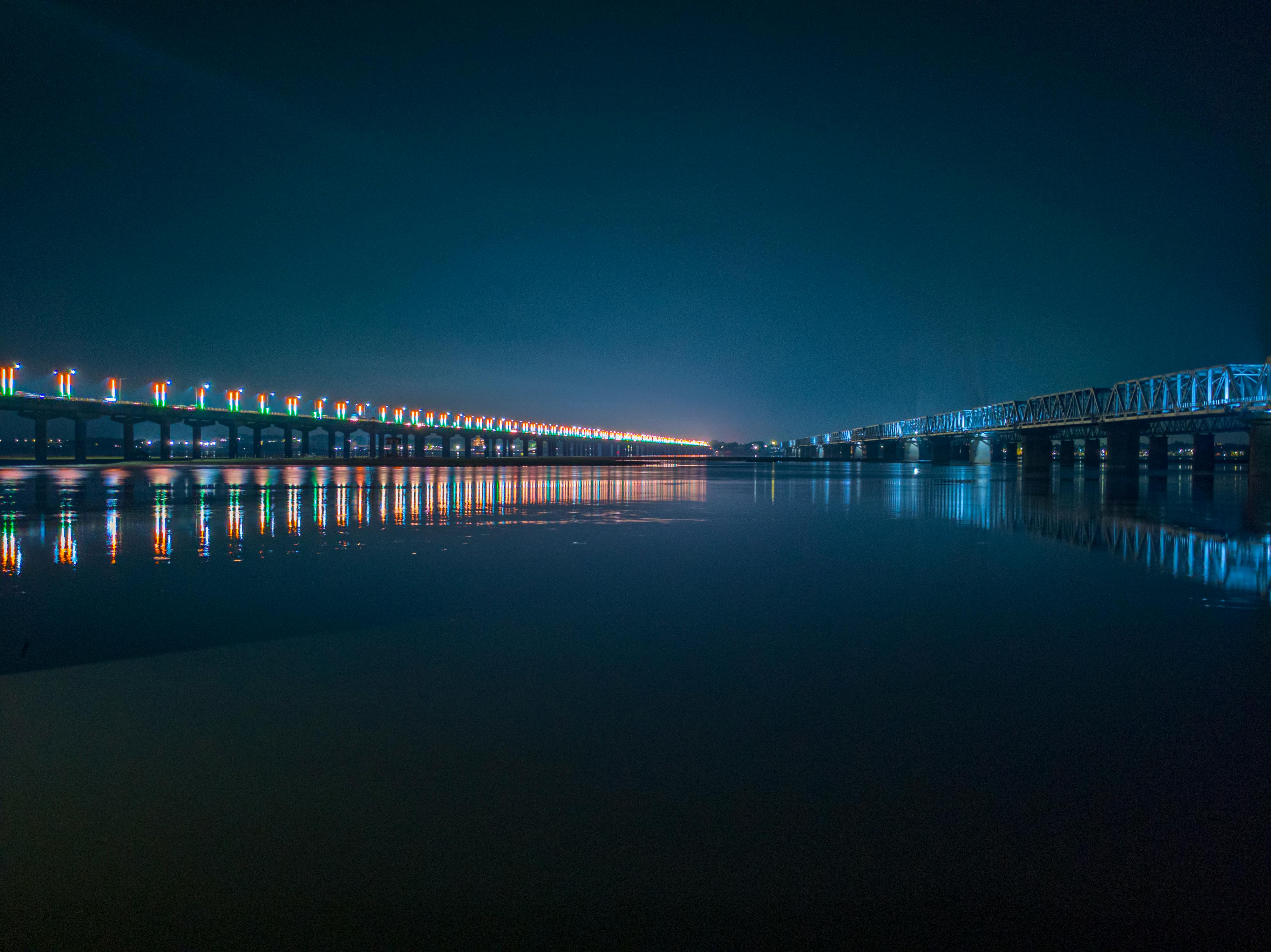 A vibrant night scene showcasing an illuminated bridge reflecting on the calm water.
