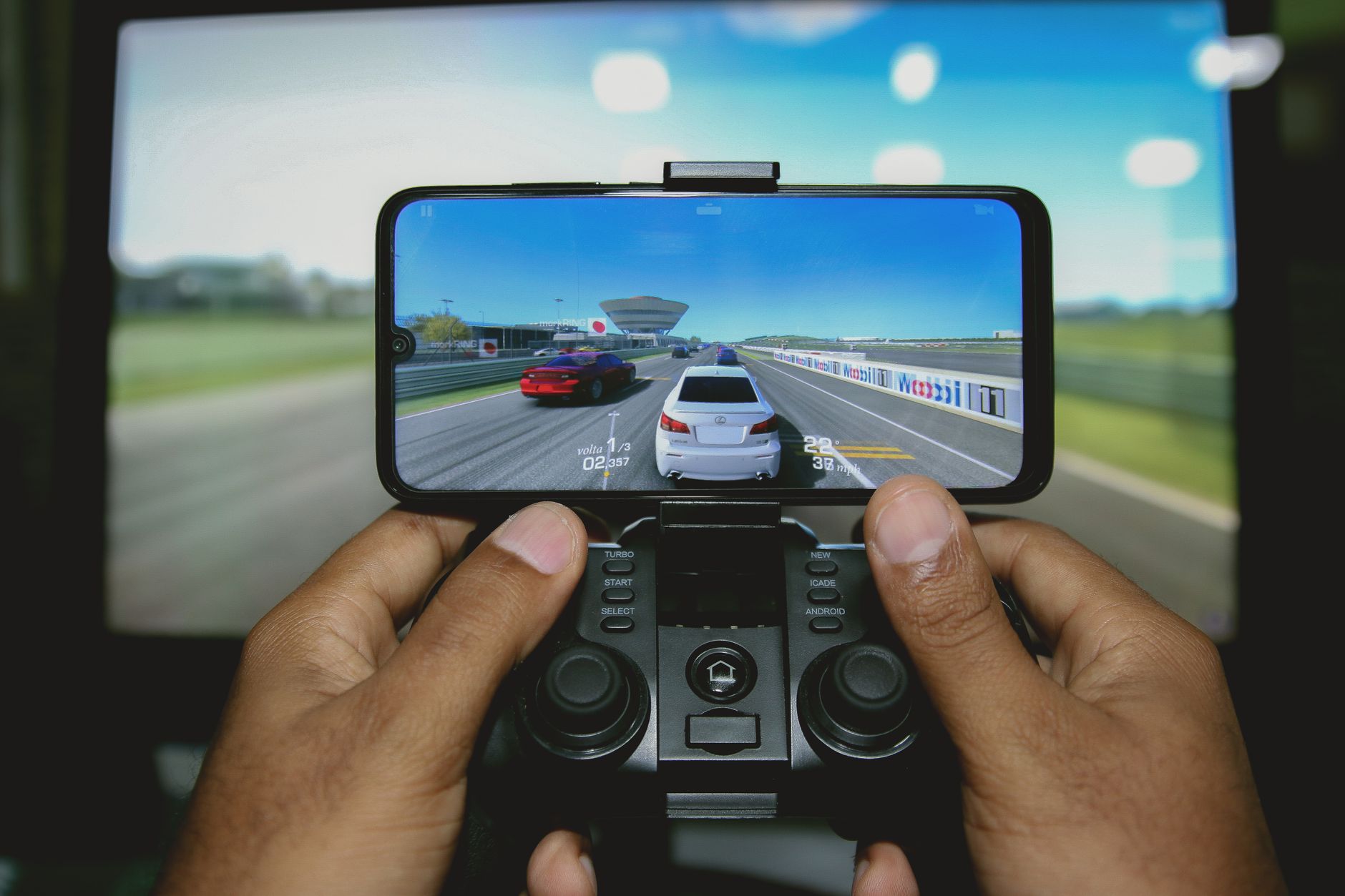 Close-up of hands playing a racing game on a mobile device with a controller.