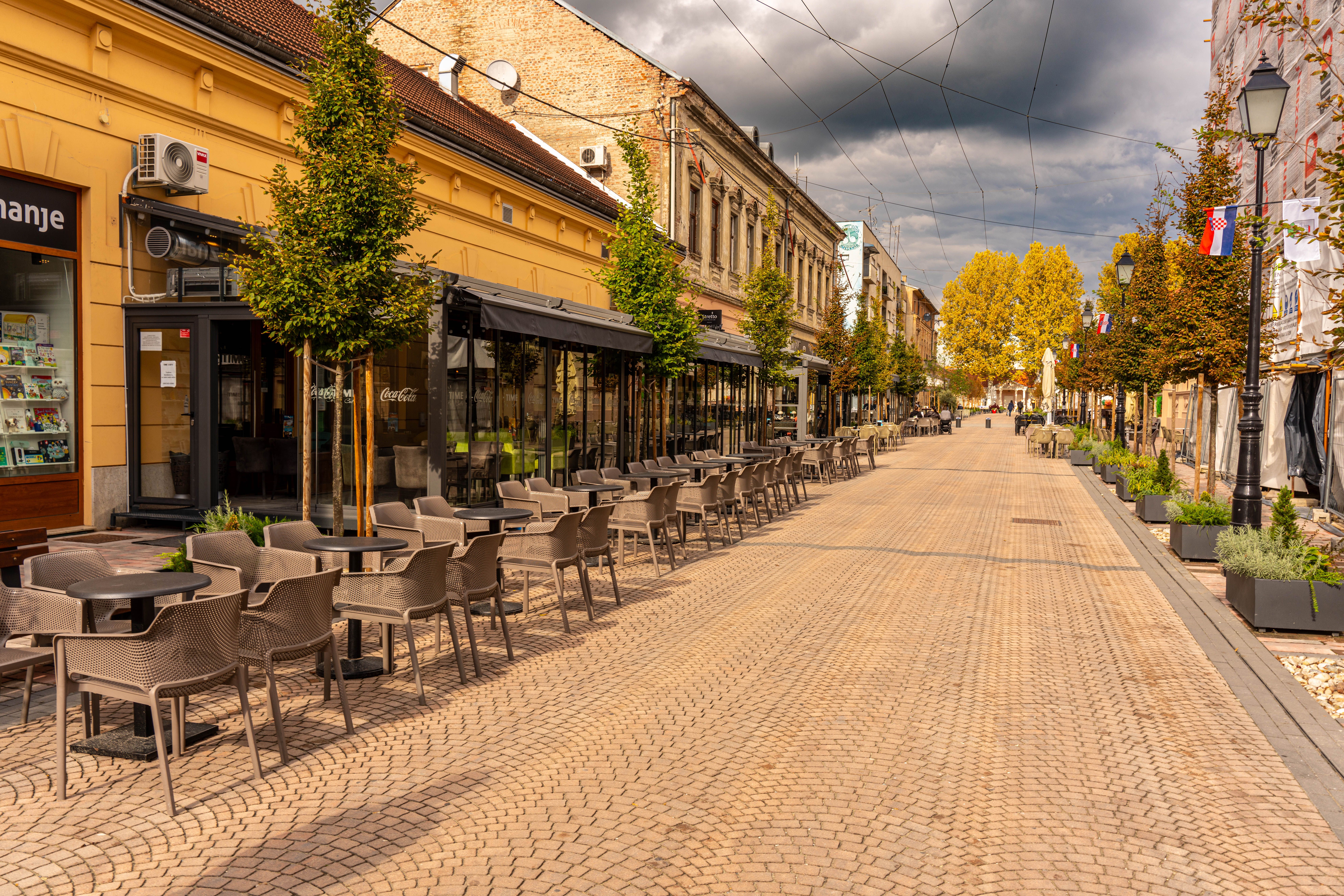 An empty street of cafe tables under autumn trees